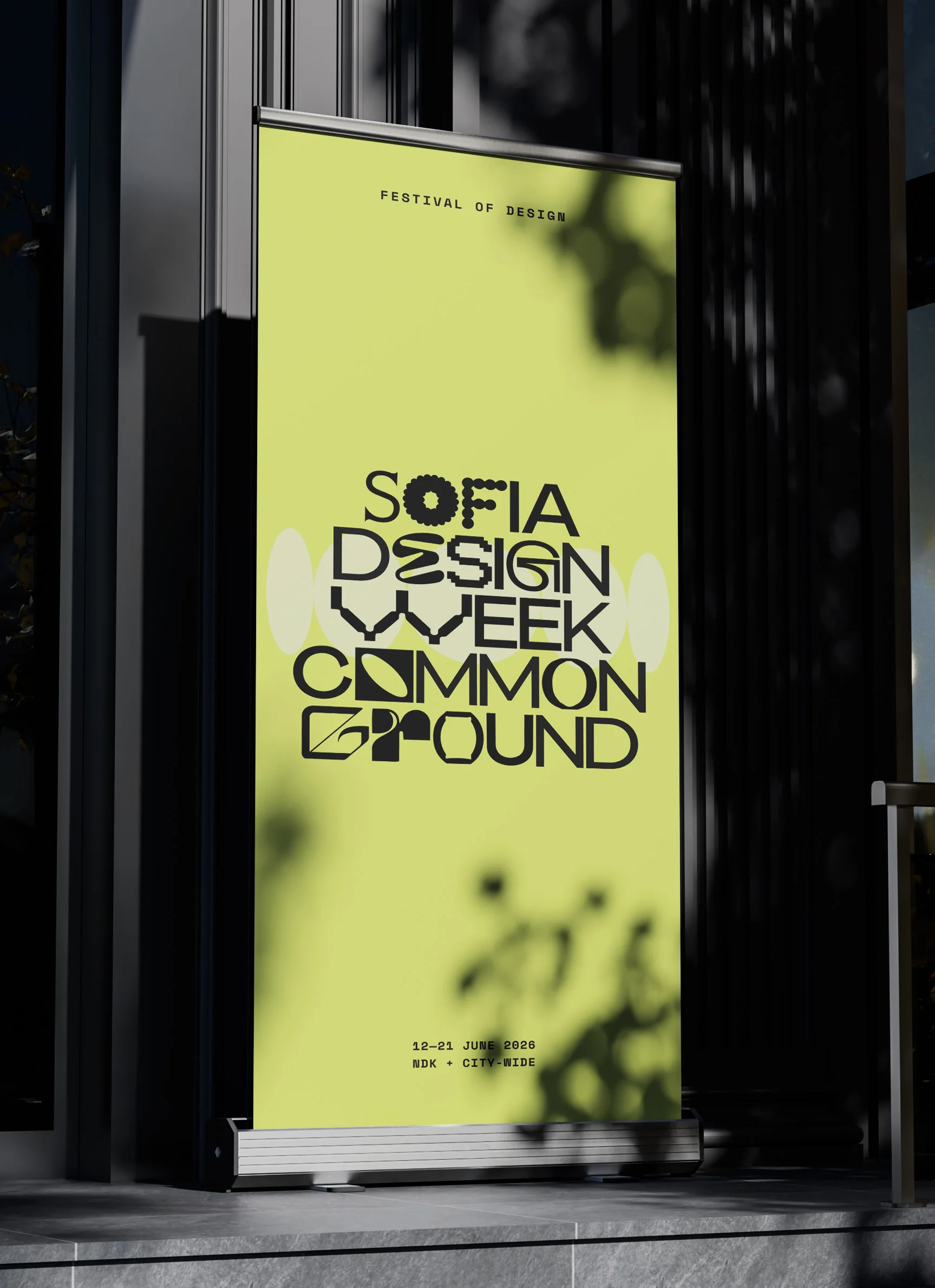 Sofia Design Week 2026 “Common Ground” poster on a roll-up banner at a building entrance — bold black display lettering on a lime-yellow ground
