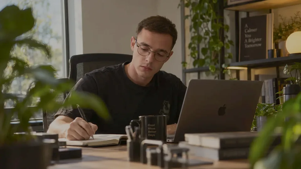Tihomir at his desk, sketching in a notebook beside a laptop